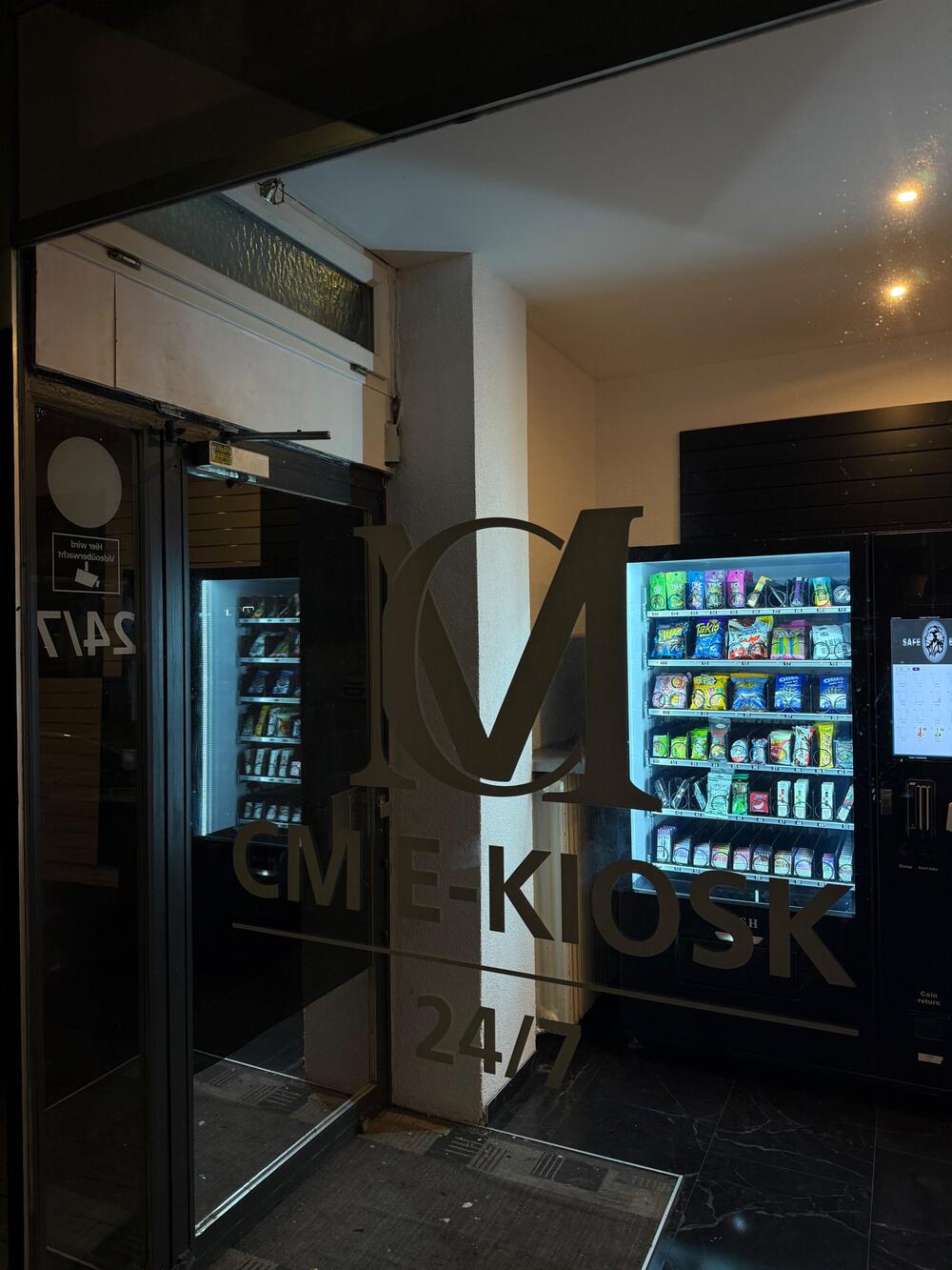 Eingang des CM E-Kiosk Pforzheim mit Logo auf der Glastür