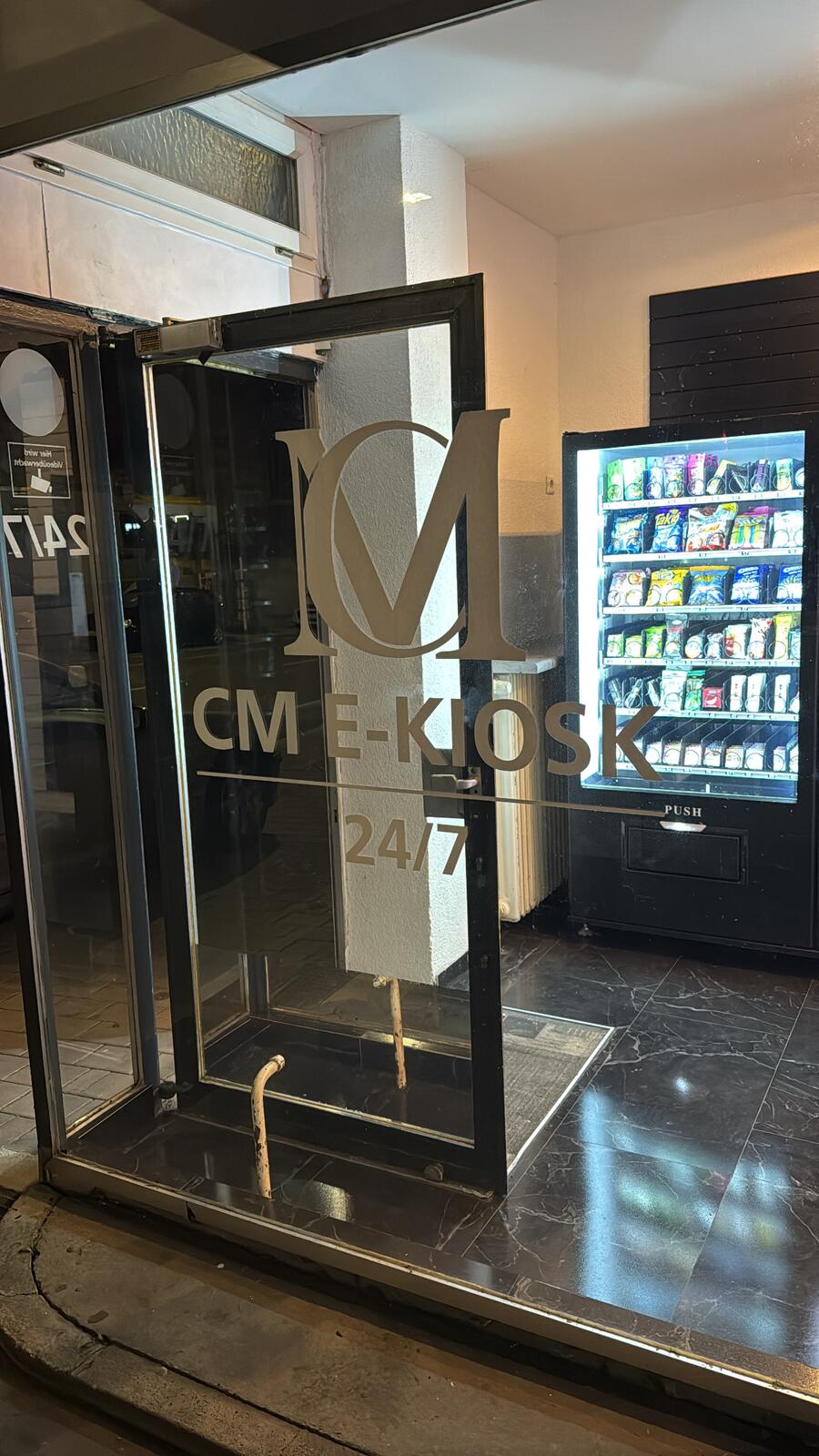 Glastür mit CM E-Kiosk Logo bei Nacht
